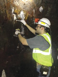 A man wearing a hard hat and a vest works in a gold mine.
