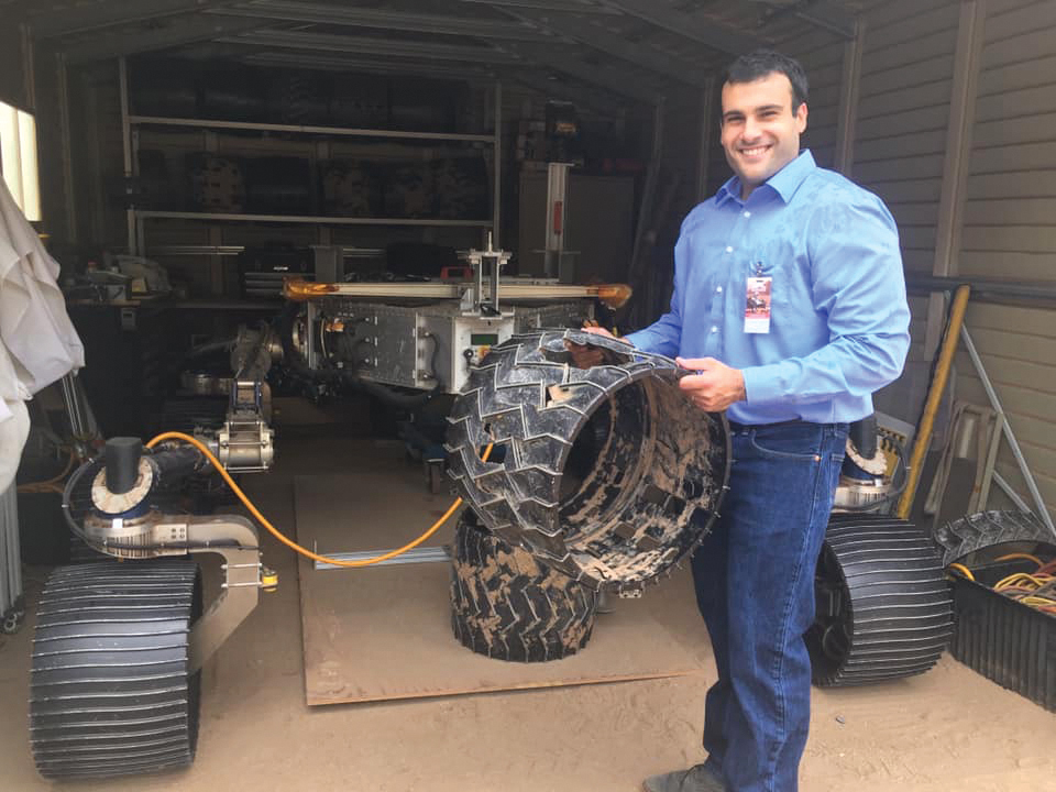 A man wearing a blue button down and jeans stands in a garage.