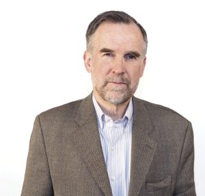 A man wears a grey suit jacket and a light blue button down.