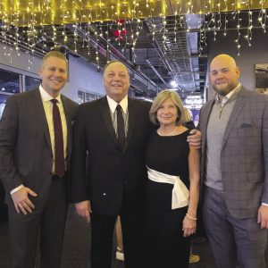 Four family members, three men and one woman, stand together inside a facility with string lights hanging from the ceiling.