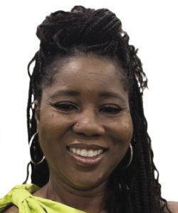 A woman with long dark braids wears hoop earrings and a yellow top.