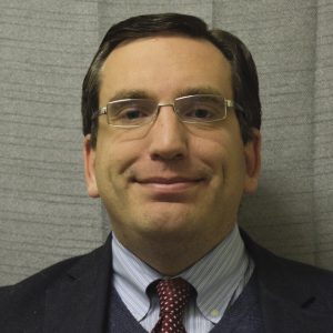 A man with short brown hair wears glasses.