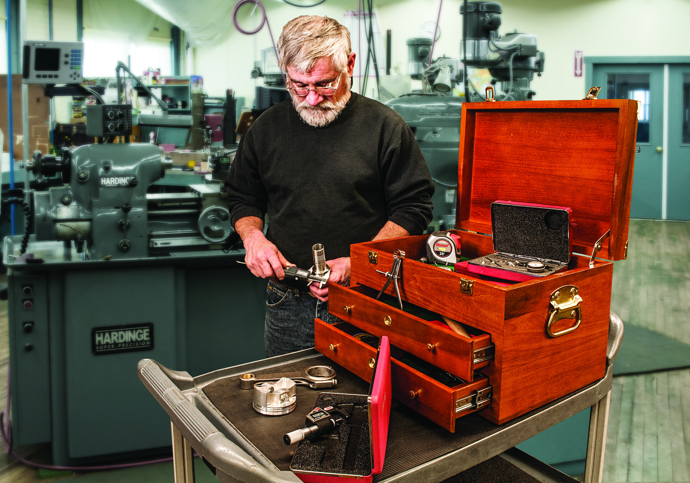 A man wearing a black sweatshirt holds tools next to a wooden toolbox