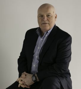 Man in suit sits for photo in front of white wall